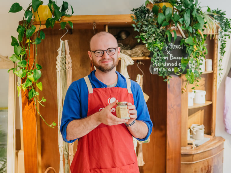 Man wearing apron holding DIY soy candle. 
